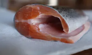 Ein Stück frisches, pinkes Forellenfilet liegt auf Küchenpapier. Die Textur des Fleisches ist deutlich erkennbar.