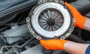 Mains gantées d'orange tenant un embrayage usé, signe d'un embrayage qui patine. Réparation automobile.