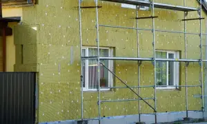 Budynek ocieplany wełną mineralną, widoczne rusztowania i okna. Tak powstaje wełna, która chroni dom.