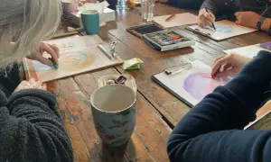 Creatieve workshop voor hsp mensen. Ze tekenen met pastelkrijt op papier, omringd door kopjes en kleurpotloden.
