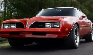 Röd Pontiac Trans Am från 70-talet, med sina karaktäristiska dubbla strålkastare och en ikonisk grill.
