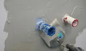 Mit einer Kelle wird graue Masse aufgetragen, um die Rohre in der Wand zu dusche abdichten.