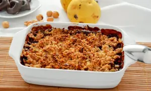 Delizioso crumble pere e cioccolato appena sfornato, con pere mature e nocciole sullo sfondo.
