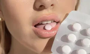 Probiotyk na nieprzyjemny zapach z ust. Kobieta kładzie tabletkę na języku, obok opakowanie.