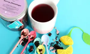Kolorowa kompozycja z herbatą dla dzieci "Berry Flamingo". Sześć małych łyżeczek z suszem owocowym, kubek z naparem i urocze akcesoria do parzenia.