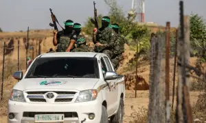 Uzbrojeni bojownicy Hamas w zielonych opaskach na głowach siedzą na białej toyocie, gotowi do akcji.