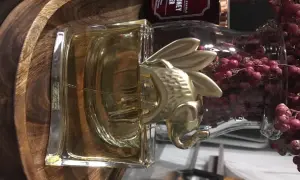 Złoty Kenzo Elephant zdobi flakon perfum, otoczony drewnianą misą i ozdobnymi gałązkami z różowymi owocami.