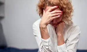 Kobieta w białej koszuli z rękami na twarzy, wyrażająca smutek. Brak współżycia konsekwencje u kobiet mogą być różne.