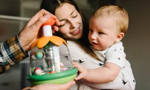 Mama i tata pokazują dziecku zabawkę. Maluch, choć nie jest jeszcze dwulatkiem, z zaciekawieniem kręci głową, obserwując kolorowe kulki.