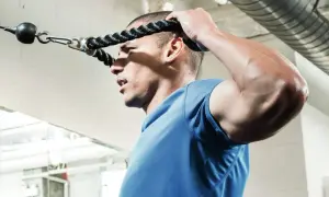 Mężczyzna ćwiczy face pull, trzymając linę wyciągu. Skupiony na prawidłowej technice.