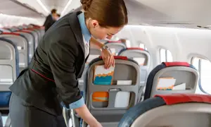 Uśmiechnięta stewardessa przygotowuje kabinę samolotu, układając materiały w kieszeniach foteli.