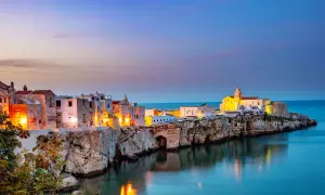 Vieste centro storico di sera, con case bianche illuminate e il mare blu che riflette le luci.