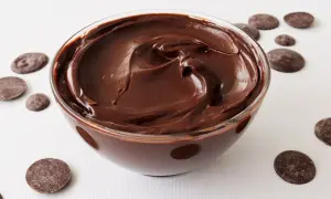 Un tazón de deliciosa crema de chocolate, con trozos de chocolate esparcidos alrededor.