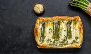 Pyszne szparagi w cieście francuskim, ozdobione tymiankiem i parmezanem, prezentują się apetycznie na ciemnym tle.