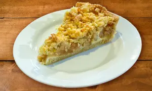 Ein Stück Apfelkuchen mit Streuseln auf einem weißen Teller. Perfekt für ein Apfelkuchen Rezept.