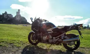 Motocykl na tle zamku i zielonej łąki w słoneczny dzień.
