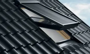 Un lucernario tetto con tenda oscurante aperta, su un tetto di tegole nere sotto un cielo azzurro.