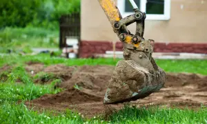 Błotnista łyżka koparki wykonuje niwelację terenu wokół domu.