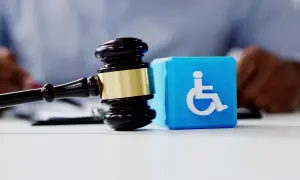 Młotek sędziowski i niebieski sześcian z symbolem osoby na wózku inwalidzkim. Symbolizuje to wniosek o wydanie orzeczenia o stopniu niepełnosprawności.