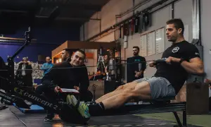 Mężczyzna trenuje na wioślarzu, podczas gdy inny mężczyzna obserwuje i notuje.