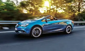 Niebieski Opel Cascada z otwartym dachem sunie po drodze, a słońce przebija się przez drzewa.