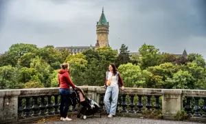 Deux femmes et une poussette devant un bâtiment avec une tour d'horloge, entouré d'arbres.