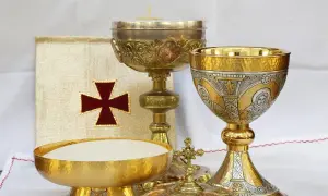 Złoty liturgiczny talerzyk z hostiami, kielichy i księga z krzyżem.
