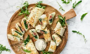 Délicieux wraps coupés en tronçons, garnis de roquette et de jambon, présentés sur un plateau en bois. Une idée simple pour une recette wrap rapide et savoureuse.