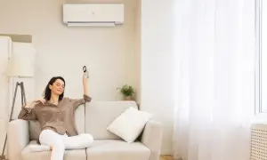 Donna rilassata sul divano, telecomando in mano, con il condizionatore acceso per una perfetta traduzione del comfort.