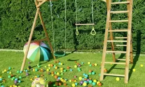 Drewniany plac zabaw ze zjeżdżalnią, huśtawką i drabinką, otoczony kolorowymi piłeczkami i parasolem.
