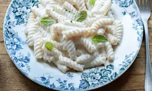 Fusilli cremosi conditi con una salsa vellutata alla ricotta, guarniti con foglie di menta fresca su un piatto decorato.