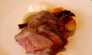 Skivad lammstek med ben, serverad med rostade potatisar, sparris, citronklyfta och en klick sås.