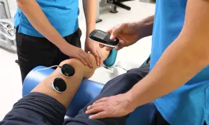 Badanie EMG: fizjoterapeuta z urządzeniem i elektrodami na nodze pacjenta.
