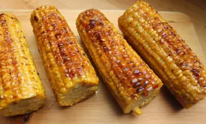 Vier Kolben zuckermais grillen, goldbraun und glänzend, liegen auf einem Holzbrett.