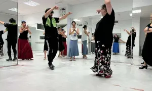 Clase de flamenco facil. Varias personas practican pasos de baile frente a espejos, con movimientos elegantes y faldas amplias.