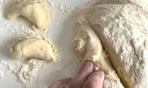 Ręce formują ciasto na pierogi, obok leżą już ulepione pierożki.