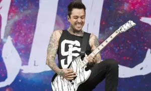 A tattooed guitarist, Tony Pierce the Veil, shreds on a white and black guitar on stage with a cosmic backdrop.