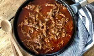 Saftigt pulled beef i en mustig sås i gjutjärnspanna, redo att serveras med träskedar bredvid.