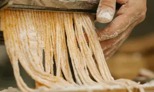Färska pastastrådar skärs från en pastamaskin, en påminnelse om vart kommer pasta ifrån.