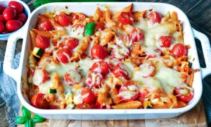 Ein köstlicher nudelauflauf vegetarisch mit Penne, Kirschtomaten und geschmolzenem Käse, garniert mit frischem Basilikum.