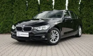 Lśniące czarne BMW 318i stoi na kostce brukowej przed żywopłotem.