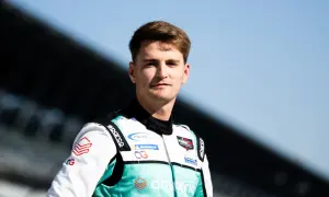 Logan Sargeant, piloto de carreras, posa con su traje de competición blanco y turquesa, listo para la acción.