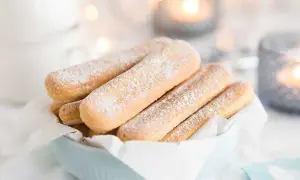 En skål med savoiardikex, pudrade med florsocker, redo för ett tiramisù-recept. Mysig stämning med ljus i bakgrunden.