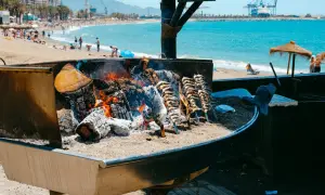 Pescado a la brasa en un chiringuito del paseo marítimo de Málaga. El mar y la playa con gente al fondo.