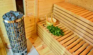 Interno di una sauna fai da te con stufa in pietra, panche in legno, secchiello e frusta di betulla pronti per un relax rigenerante.