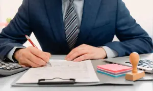 Mężczyzna w garniturze podpisuje dokumenty. Czy to rezydent, kto to? Biuro, praca, formalności.