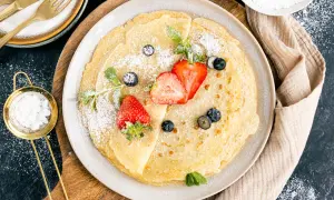 Dünne Pfannkuchen mit Hafermilch, bestäubt mit Puderzucker und garniert mit frischen Erdbeeren und Blaubeeren.