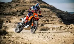 Motocyklista w kasku i stroju crossowym śmiga pomarańczowym motocyklem po pustynnym terenie. Czy na crossa trzeba mieć prawo jazdy?