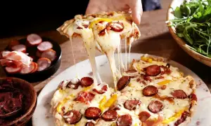 Rozciągający się ser z kawałka pysznej pizza farmerska, z kiełbasą i papryką, obok miseczki z rukolą.