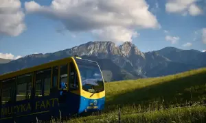 Żółto-niebieski wagonik PKL **wyciąg krzesełkowy na Gubałówkę** wjeżdża na zielone wzgórze, w tle majestatyczne Tatry.